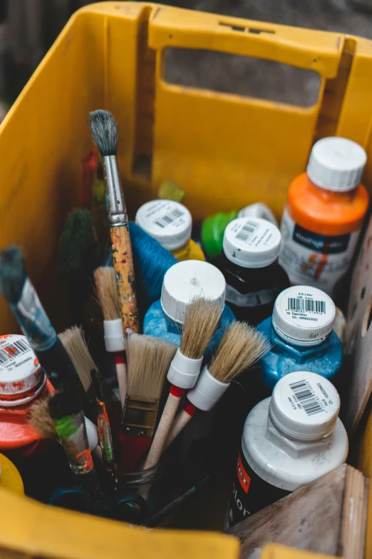 many paint and brushes sitting inside of a yellow bin