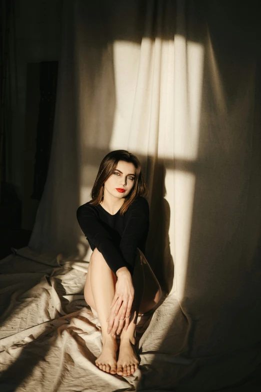 woman sitting on bed under the curtains, with light coming in on her