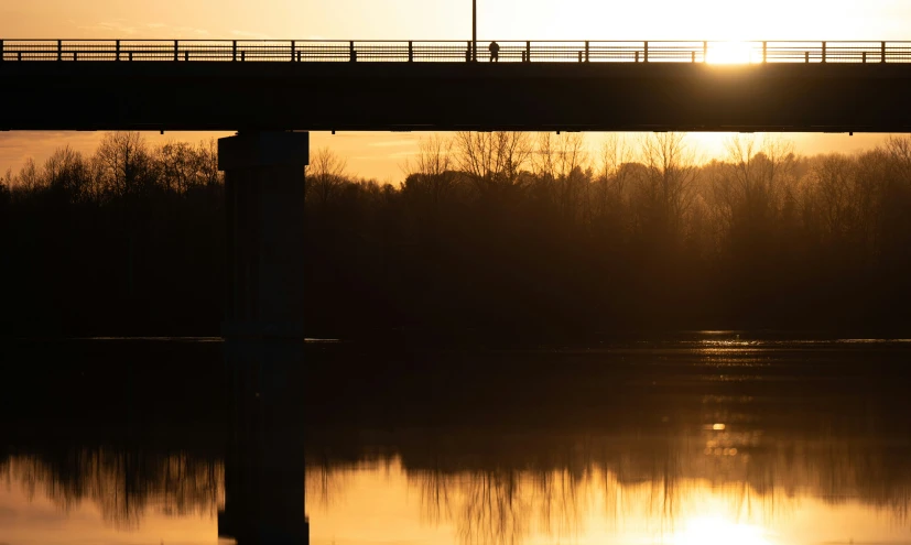a bridge with the sun setting over water
