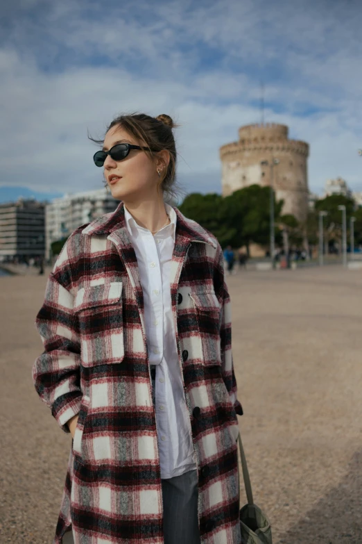 a woman wearing a coat and sunglasses posing on the beach