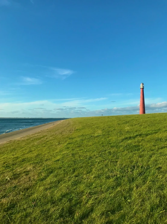 a large red object standing in a field next to the ocean