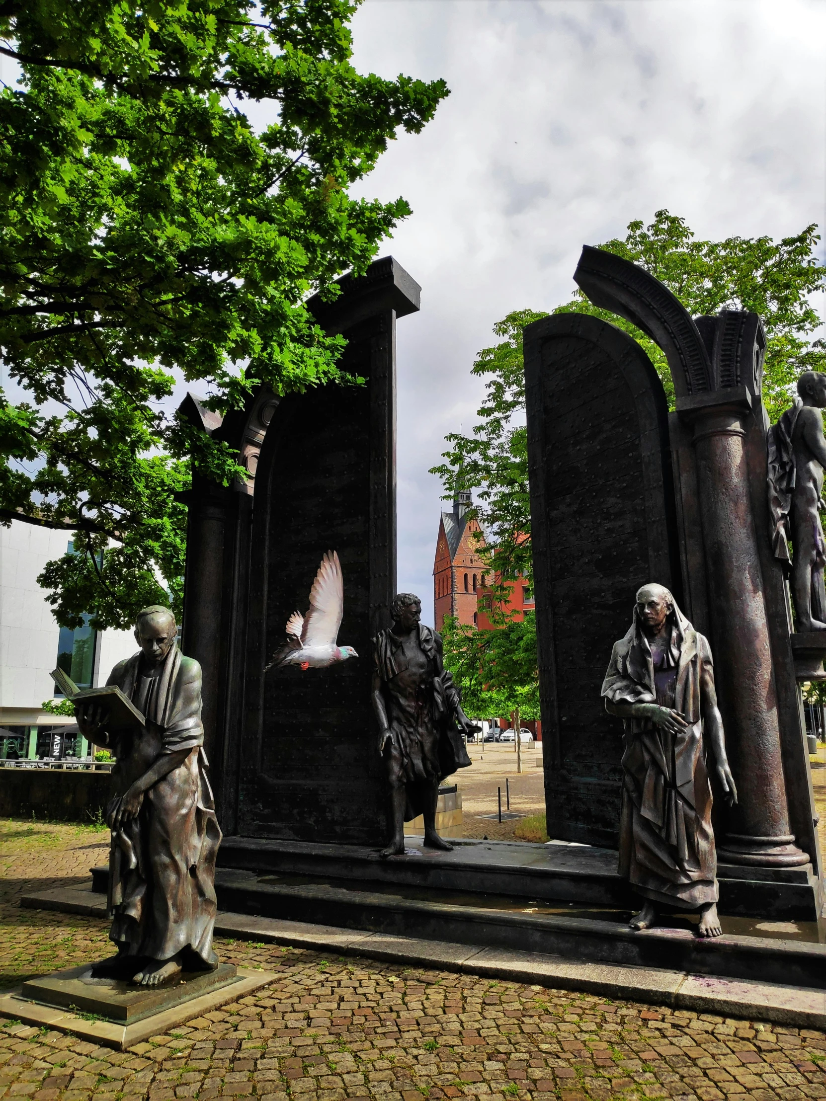 statues in a park with trees and buildings behind them