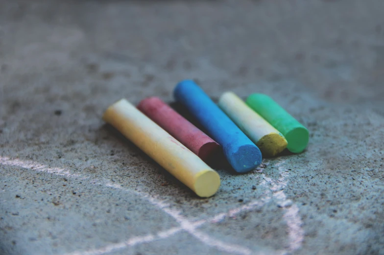 a group of four colored wood crayons are on the ground