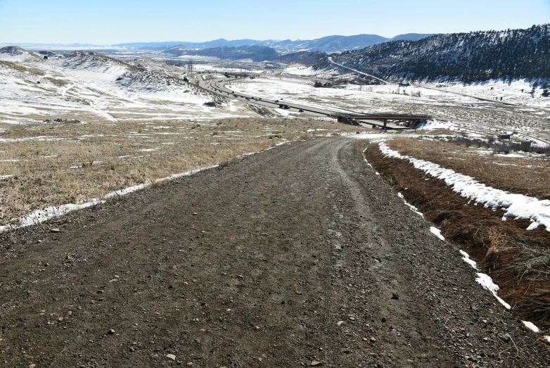 a long road near some snowy hills with trees in the distance