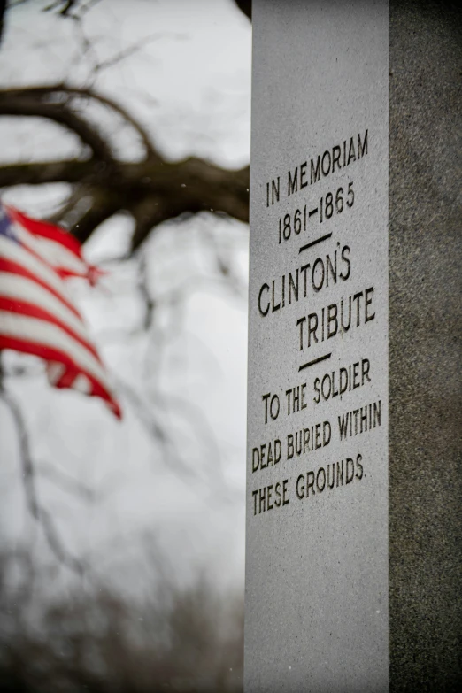 memorial marker with text on it near tree with flag