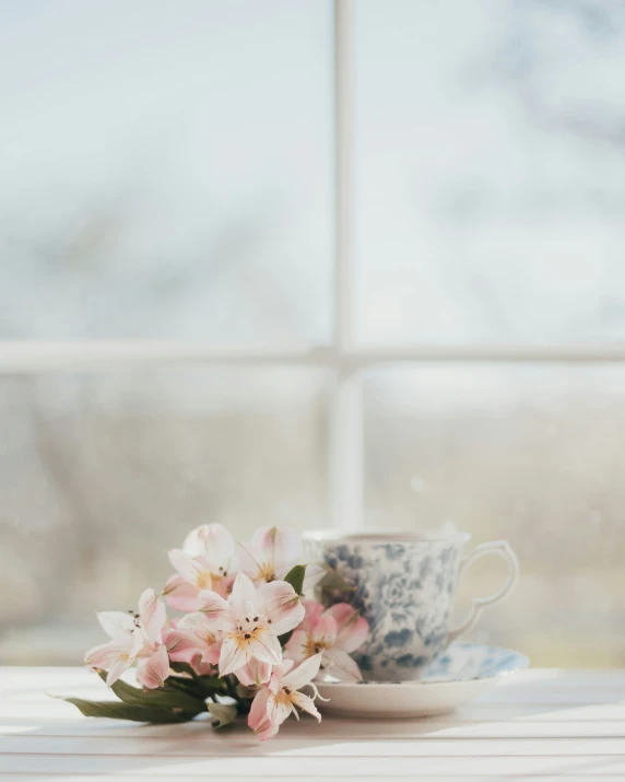 a floral arrangement sitting on a teacup in front of a window