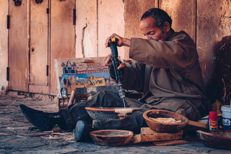 an older man sitting on the floor making some crafts