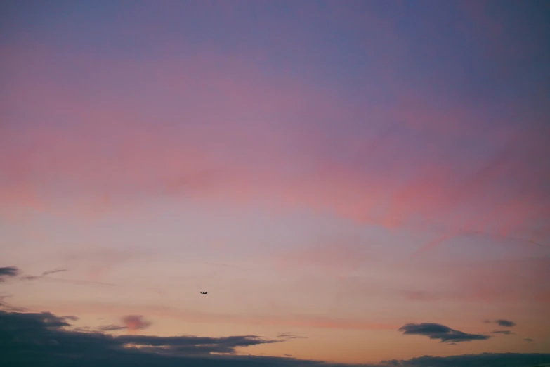 a pink sunset with dark clouds and an airplane in the sky