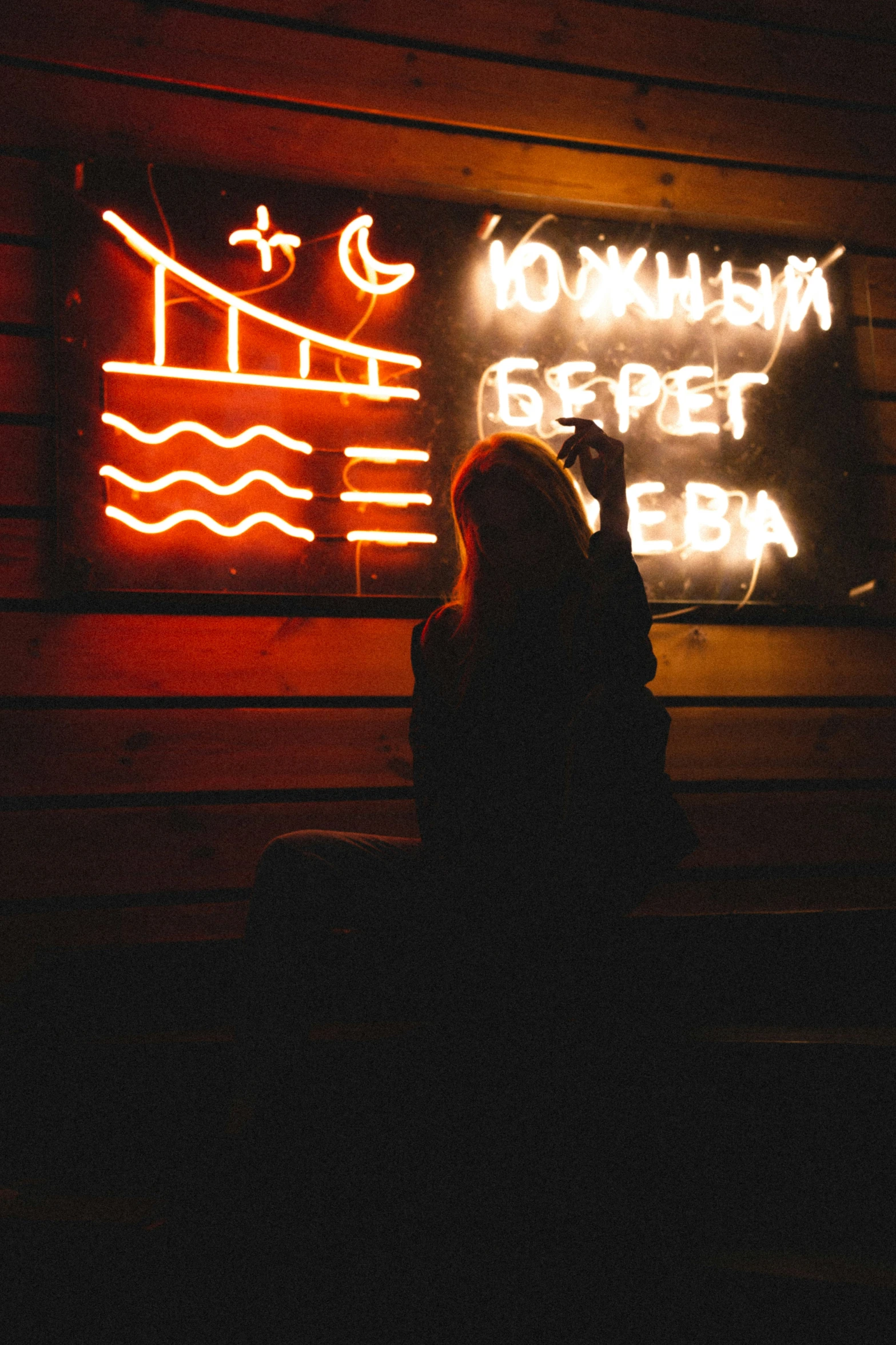 a person holding a cell phone in front of a neon sign