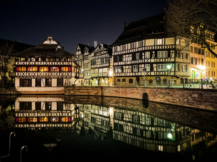 some buildings are by the water and one of them is illuminated