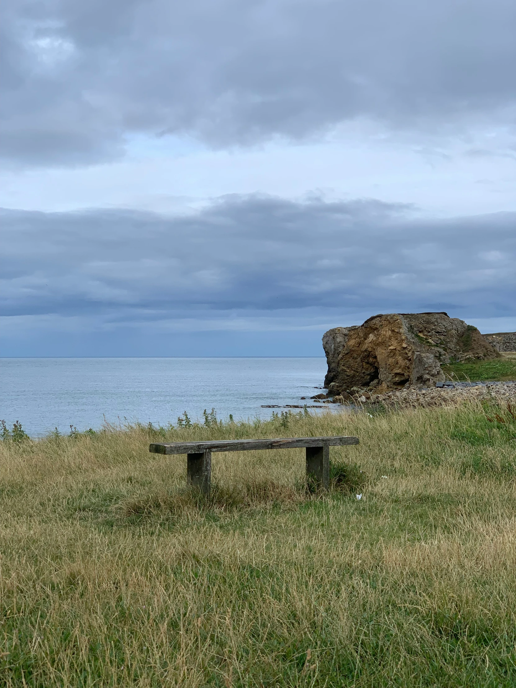 two benches are sitting in the grass by a large rock and water