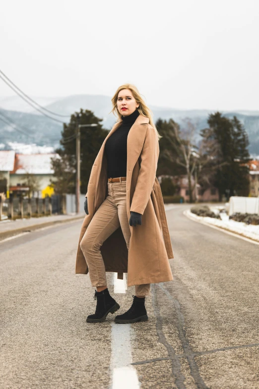 a woman in a brown coat is standing on the road