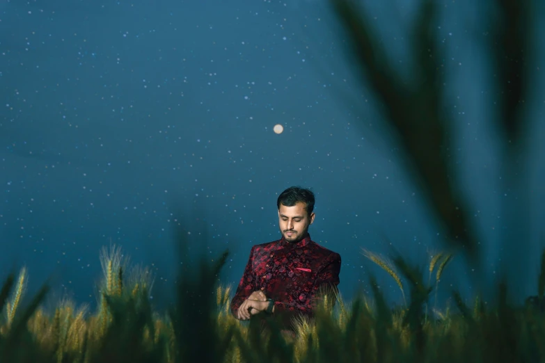 a man in a red dress stands in grass under the moon