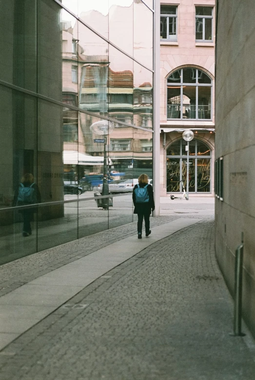 two people are walking past a building that is reflecting another person in the window