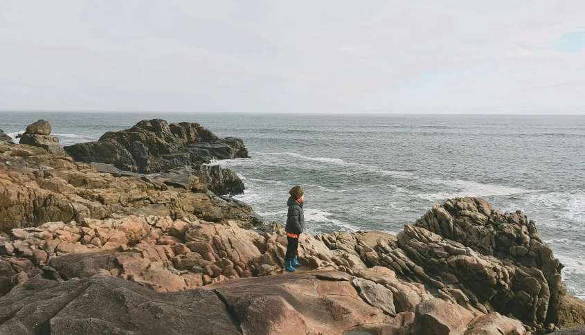 a woman stands on rocks near the ocean