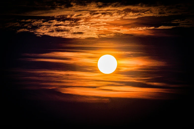 the sun setting in a dark sky with clouds