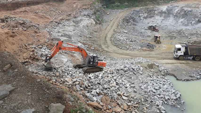 two construction vehicles are sitting on some rocks near some water