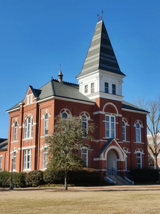 a red brick building with a steeple next to a tree and blue sky