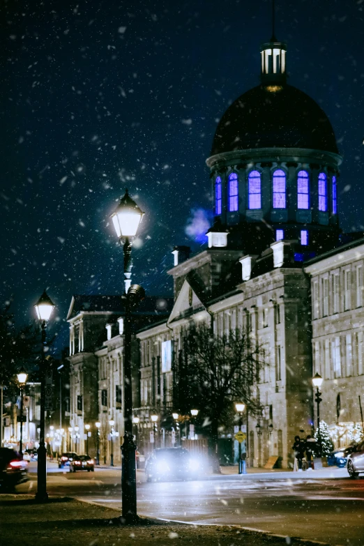 a building with a tower on the corner is lit by lights on the street and there are cars on the street below it