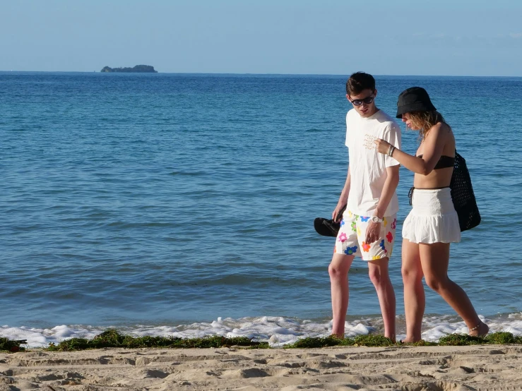 two young women wearing white at the beach looking at cell phones