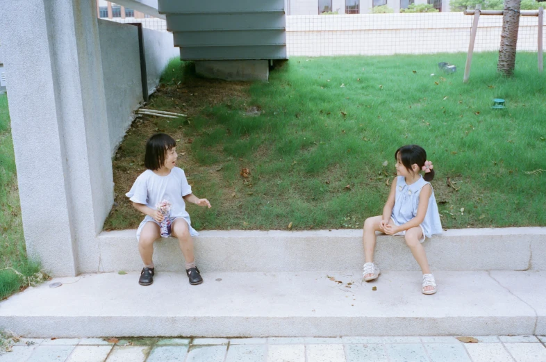 two children sitting next to each other near a grass covered yard