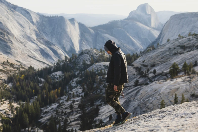 a man in camouflage gear and sneakers standing on a rock