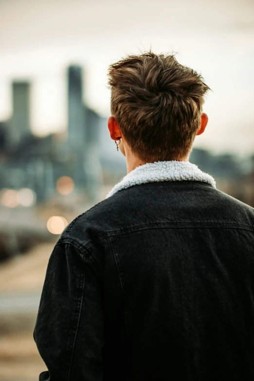 a boy wearing a black coat stands on a sidewalk