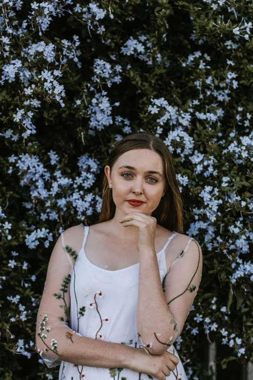 a woman with a hand on her face is standing in front of some blue flowers