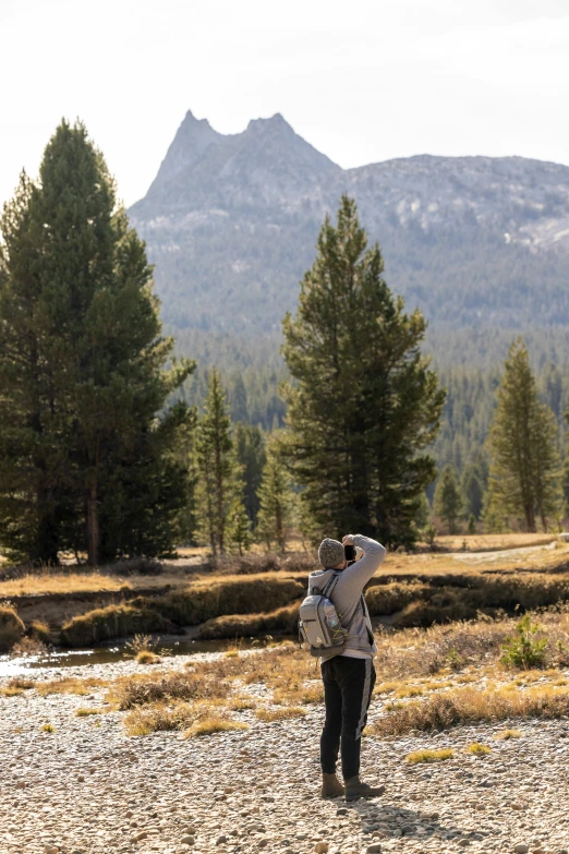 a person with a backpack standing in the grass with a mountain range behind them