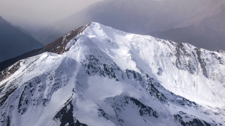 an aerial view of a snowy mountain on a cloudy day