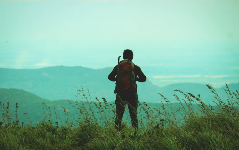 a man is standing in the grass and looking at the hills