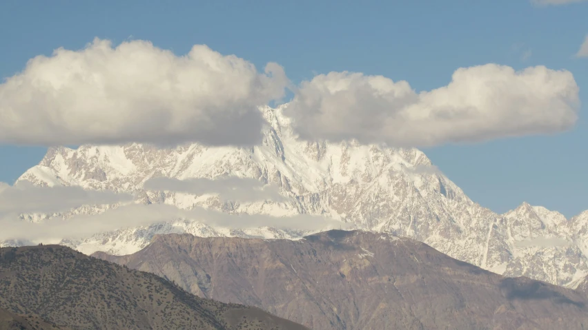 snowy mountains in front of a blue sky with white clouds