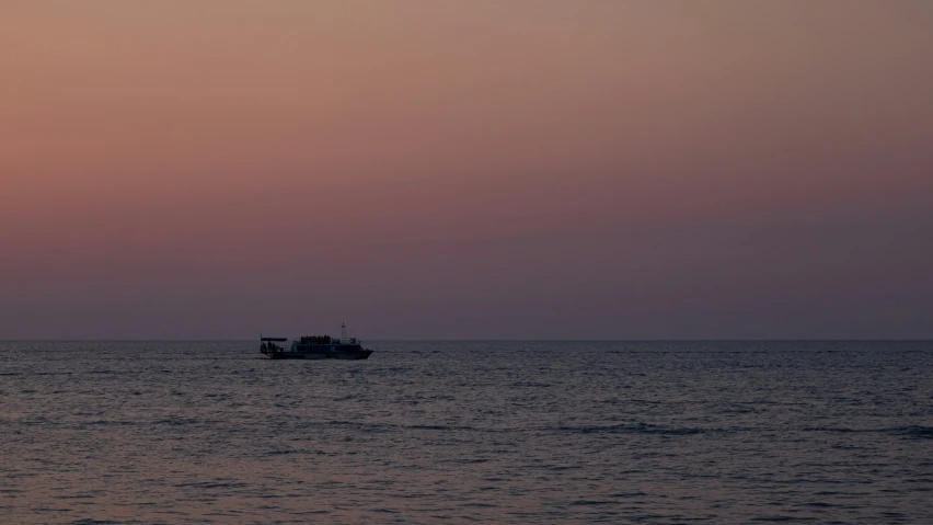 a boat traveling through the ocean under a pink sky