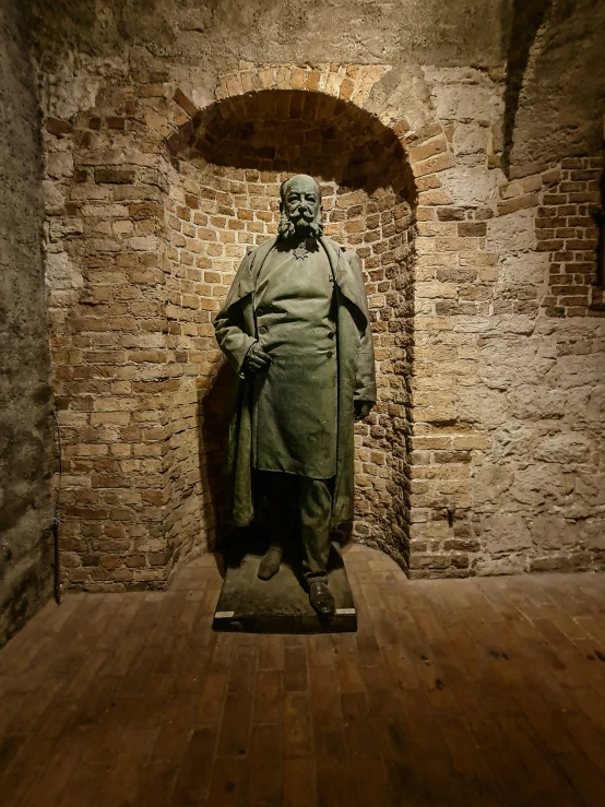 a statue of an old monk is standing on a wood floor