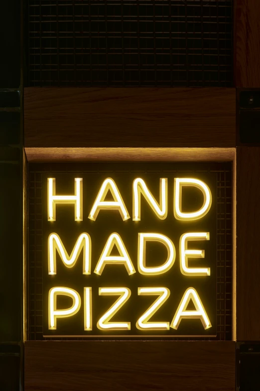 a lighted sign that reads hand made pizza on the side of a building