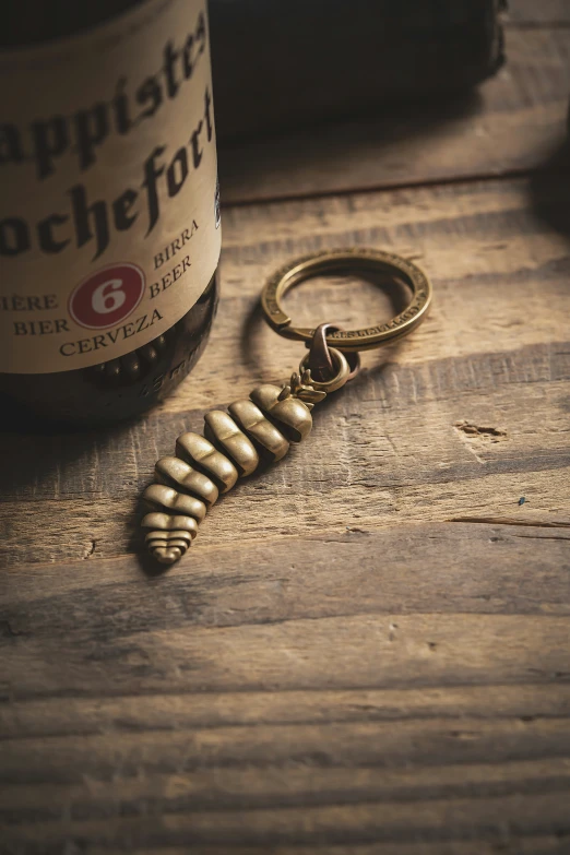 a bottle of beer and a gold - toned keychain are on the table