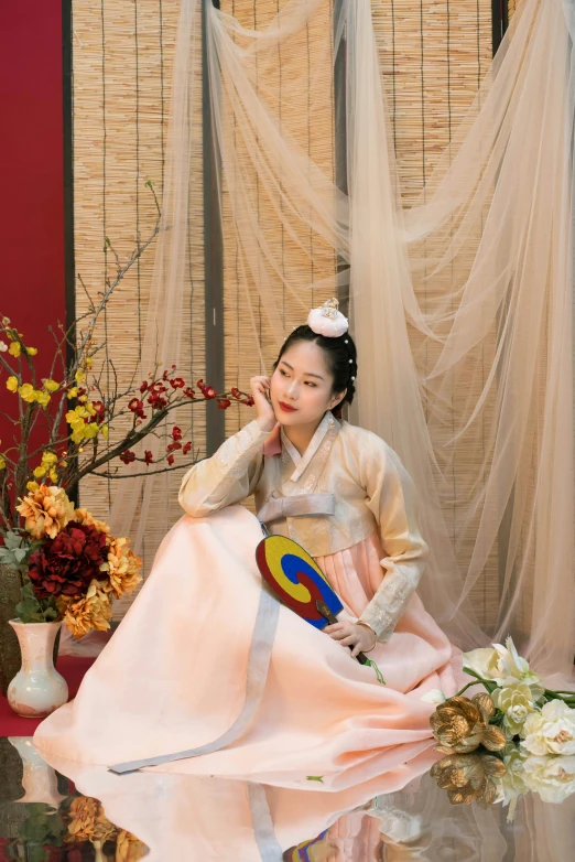 a woman in traditional korean dress is sitting in a studio