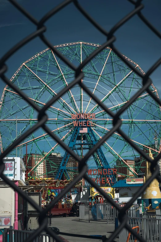 an amut park through a fence with a ferris wheel behind it