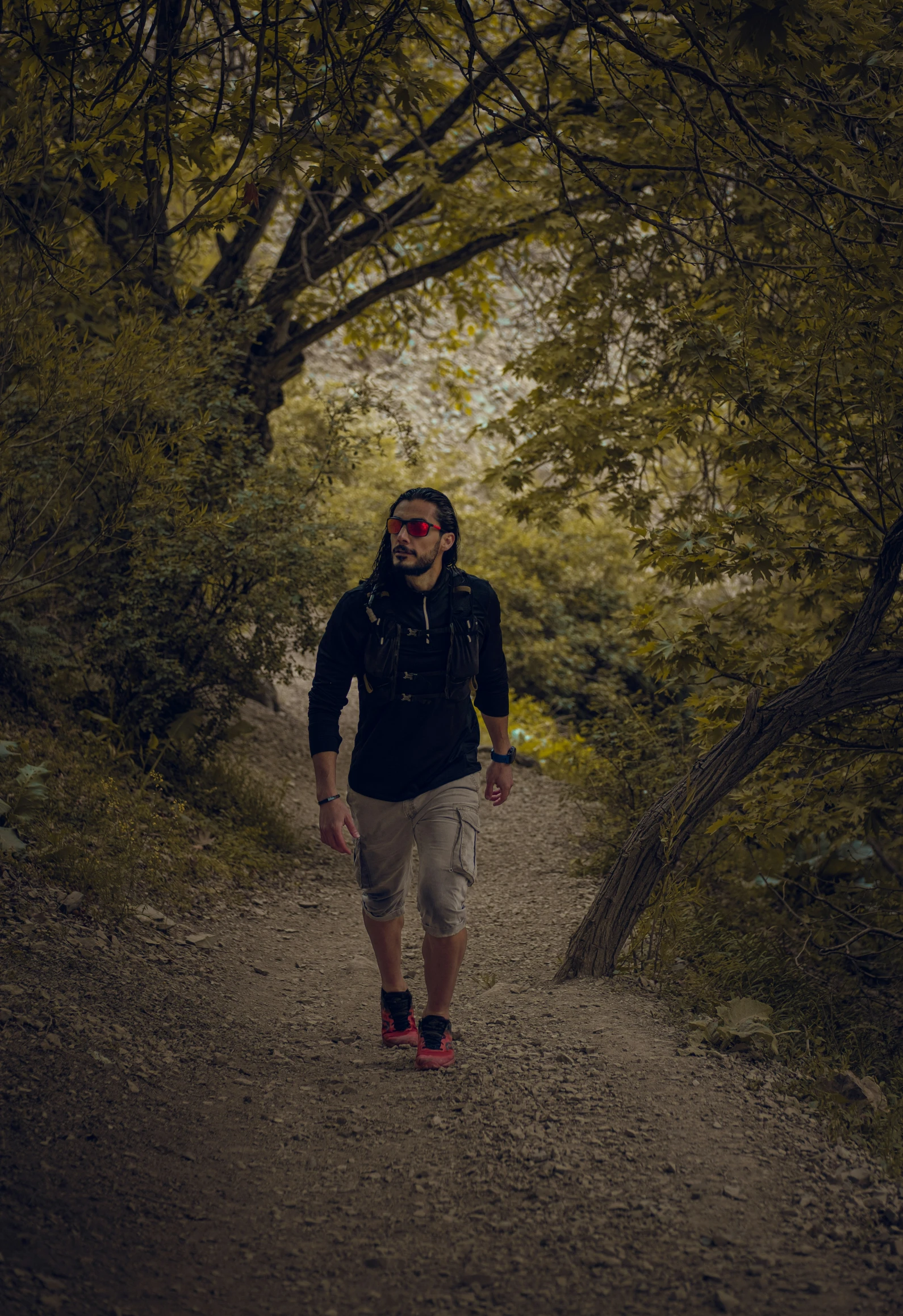 a man in shades walks through a wooded path