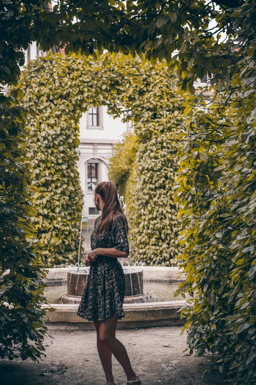 a woman walking past a fountain surrounded by trees