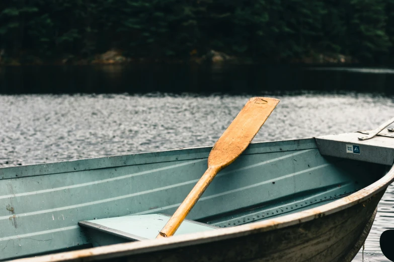 a wooden paddle rests in a long canoe on the water