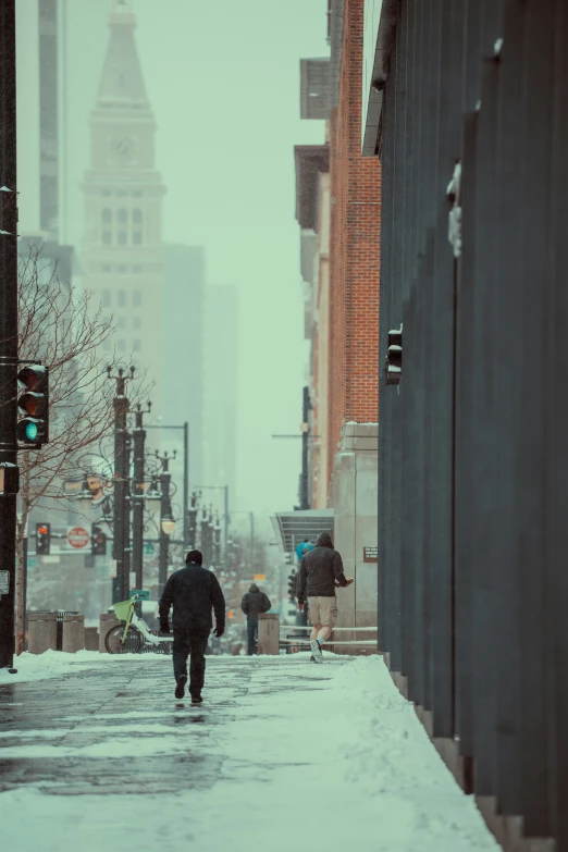 pedestrians are walking on a snowy sidewalk with tall buildings behind them