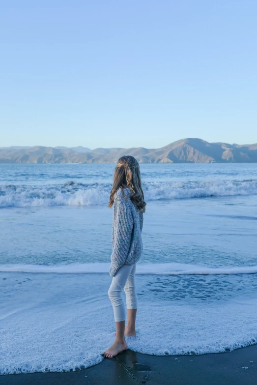 a little girl stands on the edge of the beach