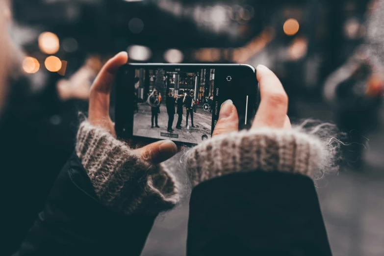 person taking a pograph with their phone of people standing on street