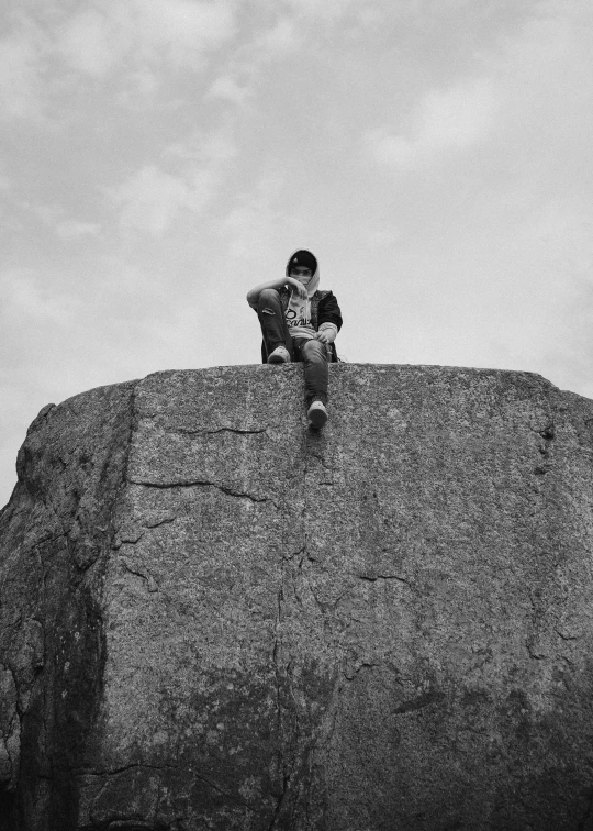 black and white po of man sitting on a large rock