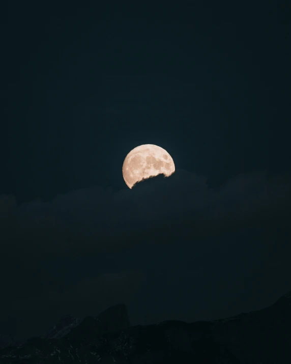 a full moon is setting over the mountains