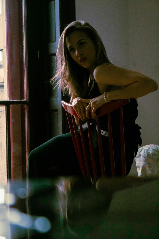 a woman sitting in a wooden chair next to a window