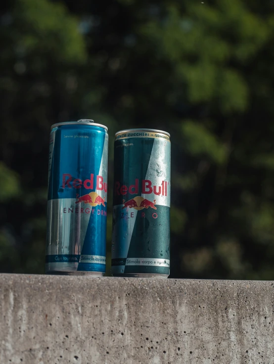 two cans of red bull sitting next to each other on top of cement