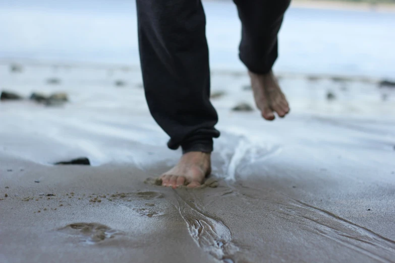 a person wearing black sweatpants walking along wet sandy beach