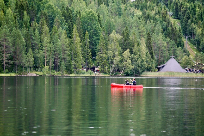 two people in a red canoe paddling along a forested lake